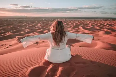 a woman sitting in the desert with her arms outstretched at Sultan Luxury Camp in Merzouga