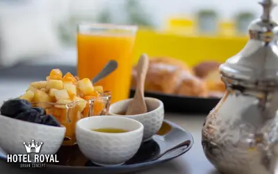 a plate of food with a bowl of fruit and a glass of orange juice at Hôtel Royal Urban Concept in Fès