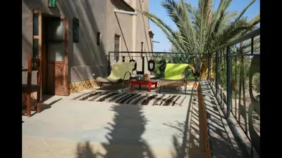 a patio with two chairs and a table and a palm tree at kasbah 123 soleil in Skoura