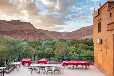 a patio with tables and chairs with mountains in the background at Hotel Awayou in Bou Tharar