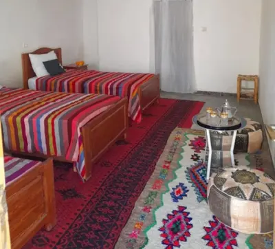 a bedroom with two beds and a table and a rug at ZEN ECOLODGE in Tighli