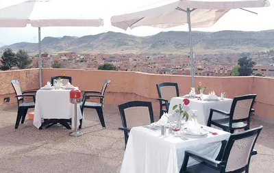 two tables and chairs with white tables and an umbrella at HOTEL CONTINENTAL Khénifra in Khenifra