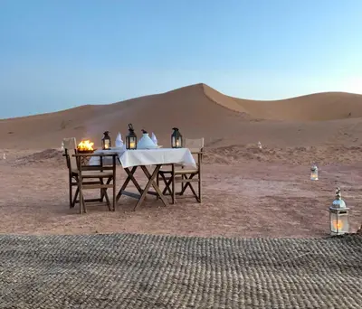 a table and chairs in the desert with a sand dune at Nomads Dunes Nest in Merzouga