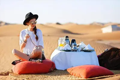 a woman sitting in the desert next to a table at Nomads Dunes Nest in Merzouga