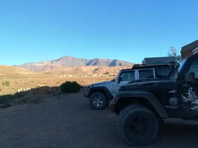 two trucks parked on a dirt road with mountains in the background at Gite Amoudou in Ouarzazate