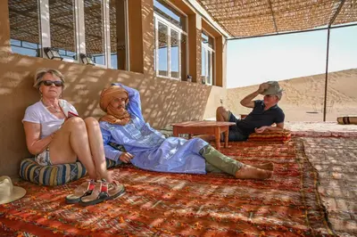 two women and a man sitting on a rug at Camp Ayour Mhamid in Mhamid