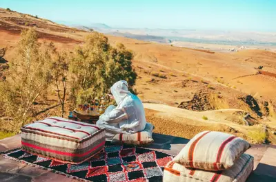 a person sitting on a blanket next to two pillows at Diar illi in Touama