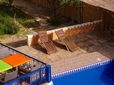 a swimming pool with chairs and a table and an umbrella at La Kasbah Elkhorbat Muxu Berbere in Asrir