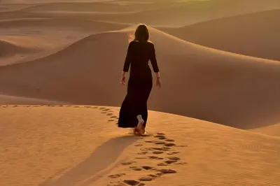 a woman walking on a sand dune in the desert at Sahara Bedouin camp in Mhamid