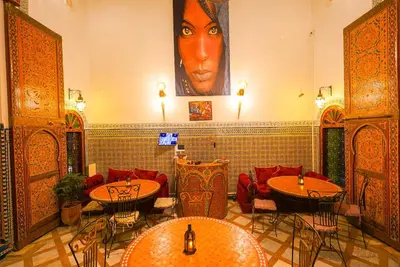 a restaurant with tables and chairs and a large painting on the wall at Riad Sahraui in Fès