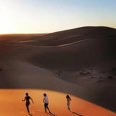 three people walking in the desert on a sand dune at Camp Cheri Beri in Mhamid