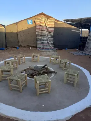 a group of tables and chairs in front of a building at Travel Oasis Merzouga Camp in Merzouga