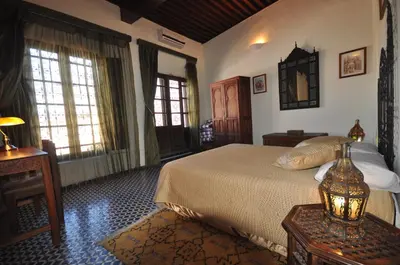 a bedroom with a bed and a table and windows at Riad Le Sucrier de Fès in Fès