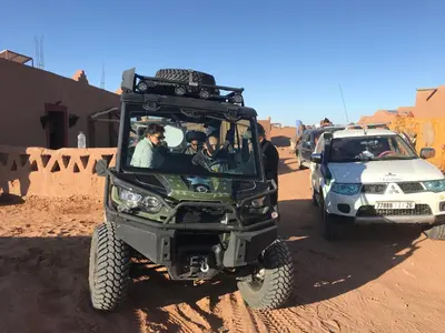 a green jeep and a white car on a dirt road at Desert Camp Laila in Mhamid