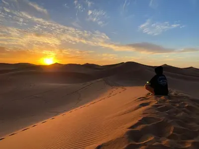 a person sitting in the desert watching the sunset at Desert Camp Laila in Mhamid