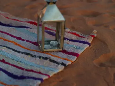 a lantern sitting on top of a striped rug at Merzouga Authentic Camps in Merzouga