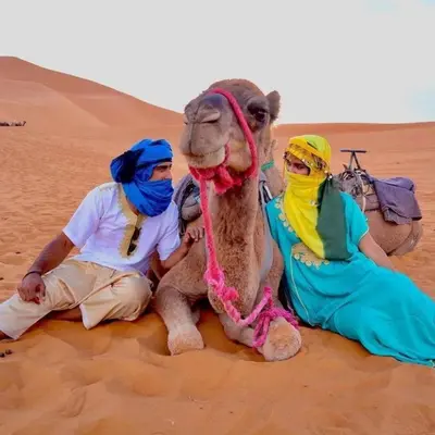 three people sitting in the desert with a camel at Sunset Camp Merzouga in Merzouga
