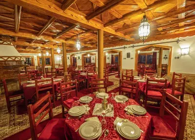 a dining room with tables and chairs and wooden ceilings at Hotel Riad Bahammou in Aït Idaïr