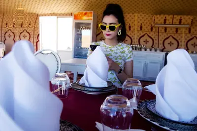 a woman wearing sunglasses looking at her cell phone at a table at ITRAN ROYAL CAMP in Merzouga