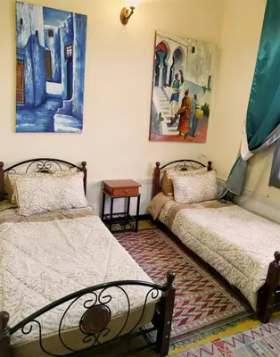 a bedroom with two beds and paintings on the wall at Maison d'hôtes Jnan Atlas in Sidi Abdalwahad