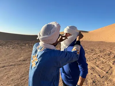 two people walking in the desert with their head covers on at Mhamid Regency Camp in Mhamid