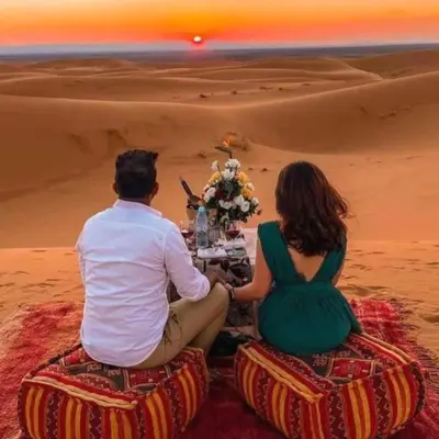a man and woman sitting at a table in the desert at Bedouin Desert Camp in Merzouga