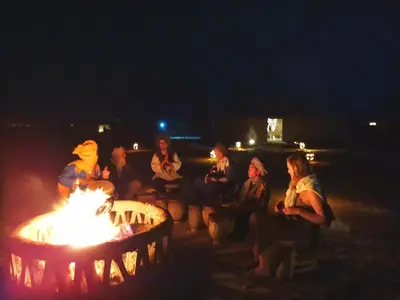 a group of people sitting around a fire pit at night at Jardin Kotori Luxury Camp in Merzouga