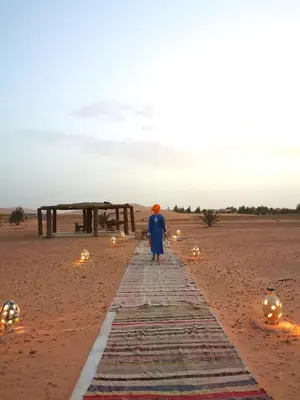 a woman walking down a path in the desert at Jardin Kotori Luxury Camp in Merzouga