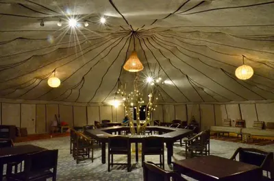 a dining room with a large tent with tables and chairs at Jardin Kotori Luxury Camp in Merzouga