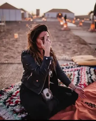 a woman sitting on the ground with her hand to her face at Merzouga Desert Luxury Camp in Merzouga
