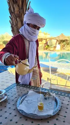 a woman is standing at a table with a drink at Dar Tafouyte in Merzouga