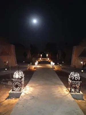 a long pathway with lights at night with the moon at RestCamp ErgChebbi in Merzouga