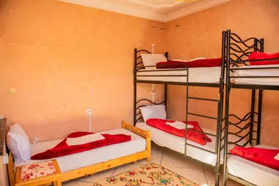 a room with three bunk beds with red sheets at Hostel Afgo Rooftop in Ouarzazate