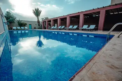 a swimming pool with chairs and blue water at Dar El Janoub in Merzouga