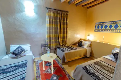 a room with two beds and a table in it at Dar El Janoub in Merzouga