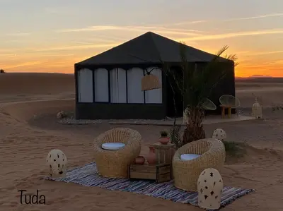 a tent in the desert with two chairs and a plant at Tuda Luxury Camp in Merzouga