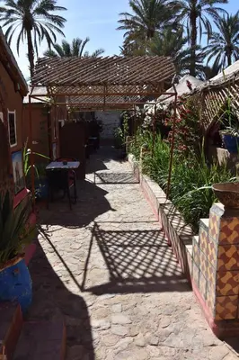 a stone walkway with a pergola and palm trees at Prends Ton Temps in Zagora