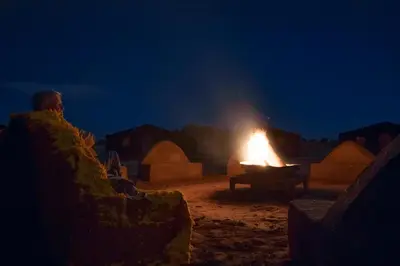 a man sitting in a chair in front of a fire at Rêve du Sahara - Dar Azawad Desert Camp in Mhamid