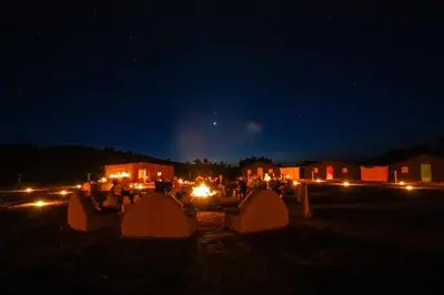 a group of people sitting around a table at night at Rêve du Sahara - Dar Azawad Desert Camp in Mhamid