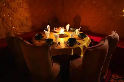 a table with chairs around it with a candle on it at Rêve du Sahara - Dar Azawad Desert Camp in Mhamid