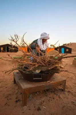 a person in the desert with a pile of sticks at Rêve du Sahara - Dar Azawad Desert Camp in Mhamid