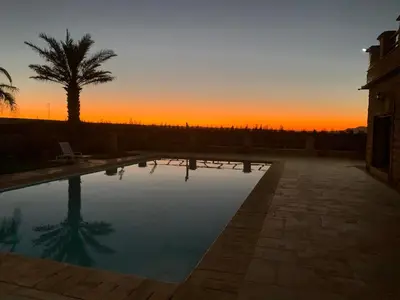 a sunset over a swimming pool with a palm tree at Villa ChezMoi in Oulad Tayeb