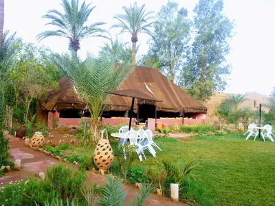 a hut with chairs and a table and palm trees at Paradise in the southern desert Morocco in Tamegroute