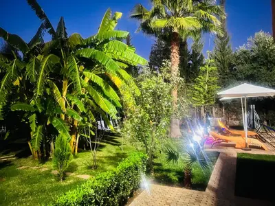 a garden with a palm tree and an umbrella at Ilafe Farmhouse, Villa avec Piscine Chauffée Privée pour Familles in Marrakech