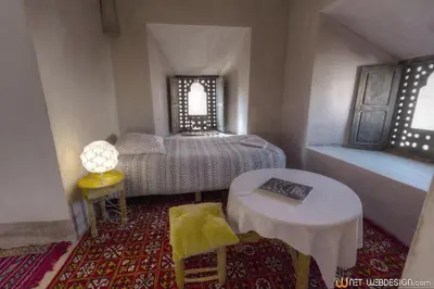 a bedroom with a bed and a table and two windows at Kasbah Agoulzi in Kalaat MGouna