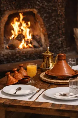 a table with plates of food and a fireplace at Casa Mona in Merzouga