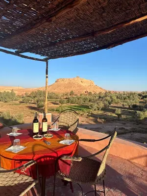 a table with wine bottles and chairs on a patio with a view at La Kasbah du Jardin in Aït Ben Haddou