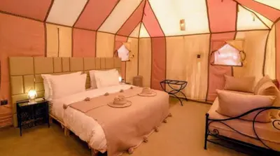 a bedroom with a large bed and a chair at Night Luxury Dunes Camp in Merzouga