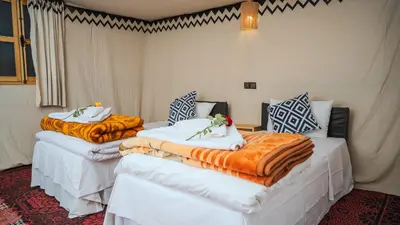 two beds in a room with orange and white blankets at Ame camp in Merzouga