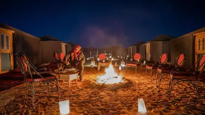 a man sitting next to a fire in front of chairs at Ame camp in Merzouga